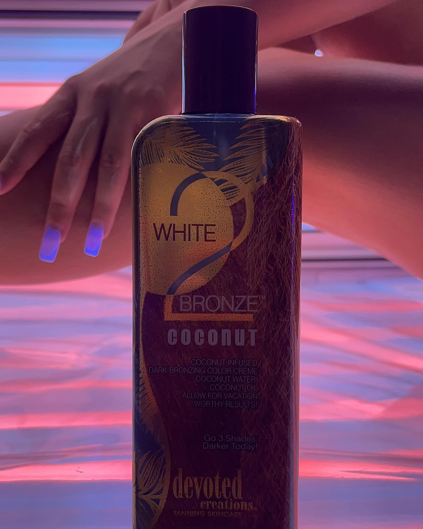 A bottle of Devoted Creations White 2 Bronze Coconut in front of sunbed tubes